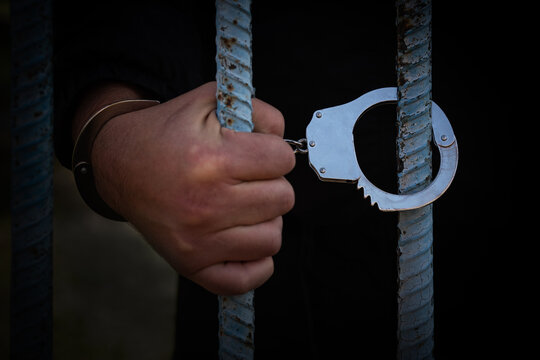 hands of prisoner with handcuff in jail as background, hands in handcuffs behind bars, man in the handcuffs is behind the bar in the police station, prisoner concept