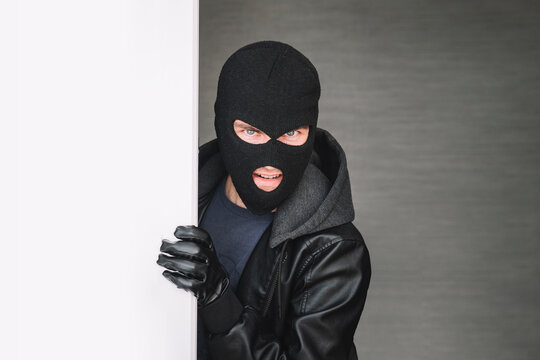 the thief looks out from around corner, copy space. thug keeps the front door Maniac broke into the room. the thief broke down the door. The evil look of the bandit on the camera. dangerous guest