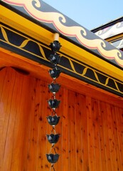Lotus flower shaped rain chain for gutters downspout against wooden building wall.