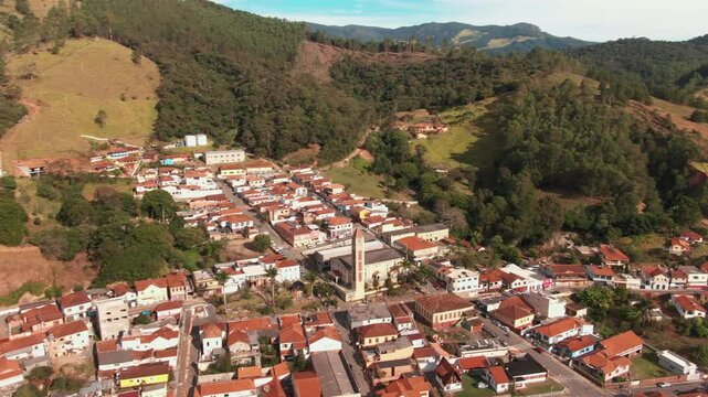Aerial panorama of Delfim Moreira, Minas Gerais, Brazil, showing a charming town with red-tiled roofs nestled among green hills and forests.