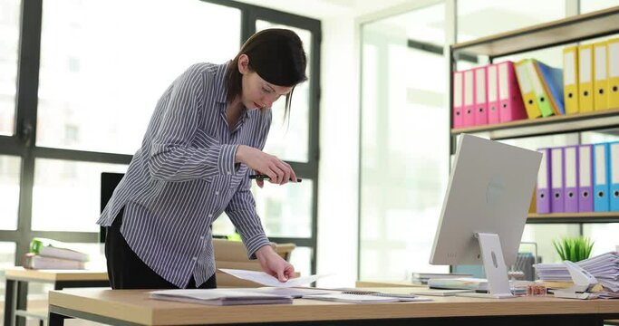 Young freelancer woman with smartphone taking photo of document report on desk to send to client