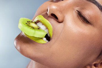 Woman, kiwi and bite with lipstick for beauty, skincare and nutrition in studio with blue...