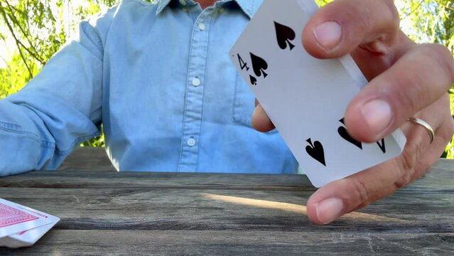 Close up hands shot of caucasian adult man sitting at the table outdoors in the park, playing cards game. Outdoor leisure activity playing board table game with friends and having fun enjoying