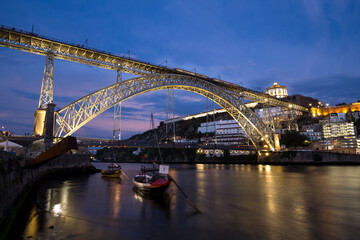 Naklejka premium Witnessing the enchanting charm of the Dom Luís I Bridge as the blue hour descends, with a passing train adding a touch of motion to the timeless scene.