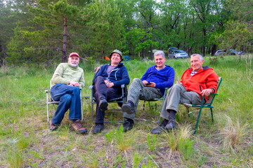 four elderly comrades resting in a clearing in the forest on a summer evening