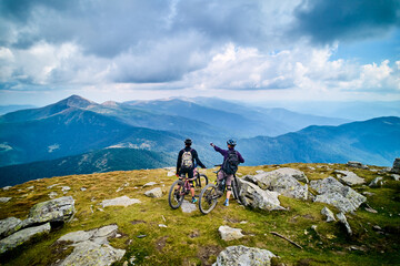 Two cyclists men riding electric bikes outdoors. Back view of male tourists resting on the top of...