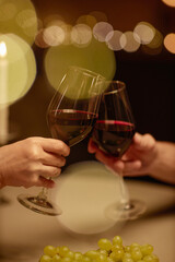 Vertical closeup of couple clinking wine glasses over table enjoying romantic dinner date with bokeh effect