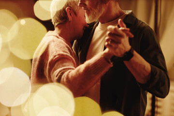 Side view of loving senior couple slow dancing and enjoying romantic date night with bokeh effect...