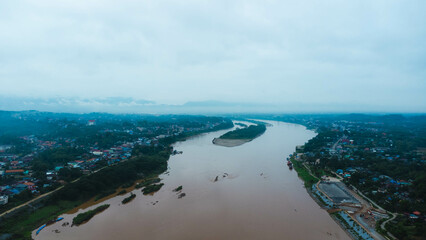 Obraz premium Aerial view of the mighty Mekong River winding from Chiang Khong, showing the vastness and beauty of the muddy waterway contrasting with the surrounding lush mountains and Laos villages.