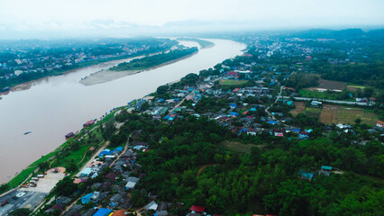 Aerial view of the mighty Mekong River winding from Chiang Khong, showing the vastness and beauty of the muddy waterway contrasting with the surrounding lush mountains and Laos villages.