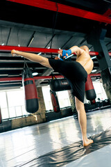in a boxing fight club bald young boxer with tattoos in blue bandages trains a kick before a fight...
