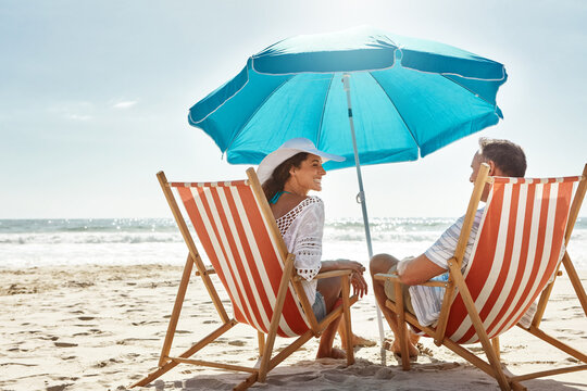Couple, relax and beach chairs with umbrella on sand for vacation, holiday or weekend break. Summer, man and woman together in nature with water for peace, travel or tourism in Bali getaway with view