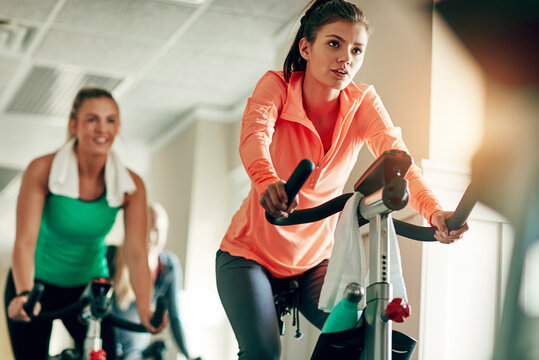 Woman, cycling and workout with spin class at gym for cardio exercise or indoor training together. Active female person or group of cyclists riding on equipment or bicycle for fitness at health club