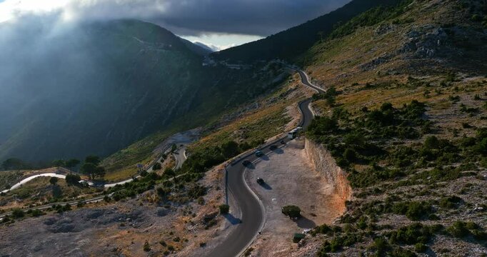 Aerial view tracking a bus and queue of cars on a mountain road, in sunny Albania