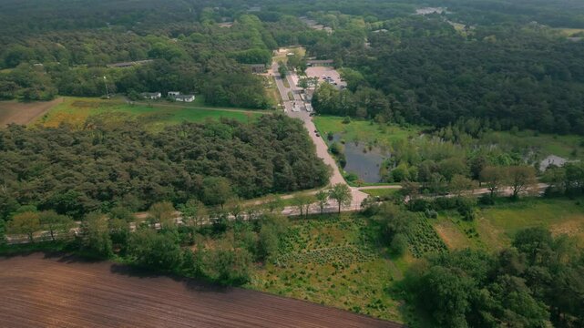 Aerial view approaching Budel Cranendonck asylum center nestled in a dense forest, highlighting its secluded location. Location: Budel, Netherlands (
