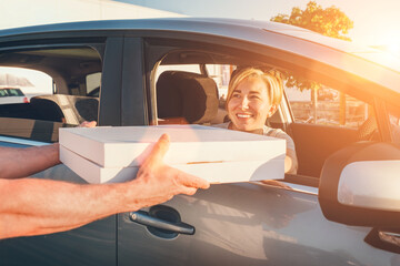 Young female sitting in car driver seat and sincerely smiling to deliveryman accepting two pizza boxes on the city street. Small business, people relations, fast foot meal consumption concept photo