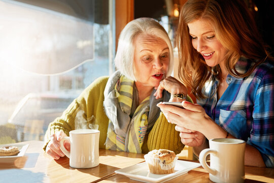 Smile, senior woman and daughter browsing smartphone in cafe for memories with social media with relax. Funny, post and tech savvy in restaurant with coffee, muffin and sunshine in retirement.