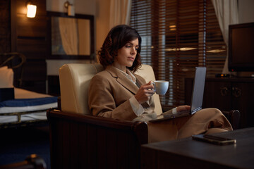 Stylish businesswoman typing laptop keyboard while resting in hotel room