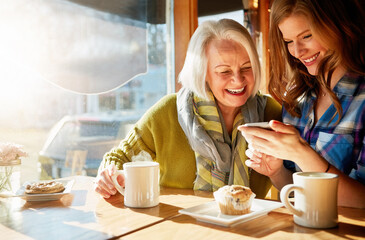 Senior woman, daughter browsing and smile with smartphone in cafe for memories with social media. Funny, post and relaxing in restaurant with coffee, muffin and sunshine in retirement with excited.