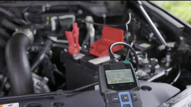 Man is measuring voltage of AGM battery power on suv car by battery tester at home.