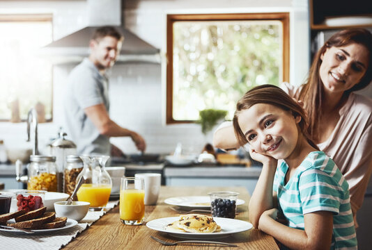 Happy, family and kid with breakfast in kitchen for healthy diet, support and child development. Smile, mother and father with little girl with food at home for nutrition, love and care on weekend