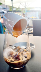 A glass of coffee with ice cubes and a cup over it