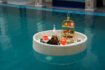 Luxurious floating breakfast tray with drinks and snacks in a swimming pool, perfect for a relaxing vacation morning. Floating Poolside Breakfast Tray with Drinks