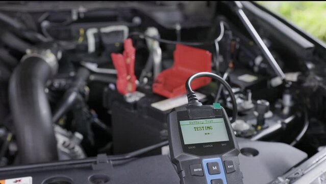 Man is measuring voltage of AGM battery power on suv car by battery tester at home.