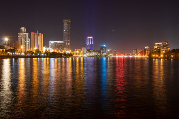 Fototapeta premium Beautiful night cityscape. View of skyscrapers. Street lighting and night illumination of high-rise buildings. Multicolored reflections in the water. Yekaterinburg city, Sverdlovsk region, Russia.