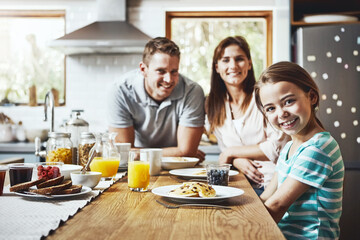 Morning, breakfast and portrait of family in kitchen for nutrition, growth and child development. Happy, father and mother with little girl by home table for healthy diet, food and care on weekend
