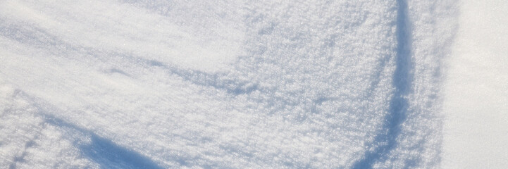 Fototapeta premium Beautiful winter background with snowy ground. Natural snow texture. Wind sculpted patterns on snow surface. Wide panoramic texture for background and design. Closeup top view with copy space.