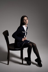 Portrait of attractive caucasian young brunette woman in school uniform sitting on chair in studio....