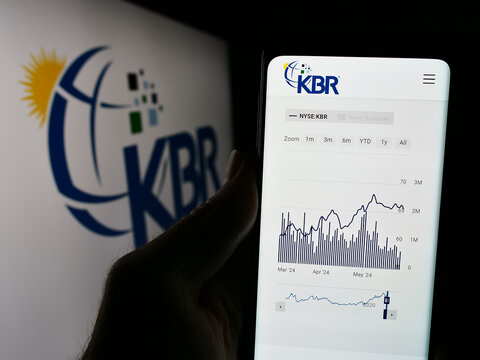 Stuttgart, Germany - 05-27-2024: Person holding cellphone with webpage of US engineering and construction company KBR Inc. in front of logo. Focus on center of phone display.