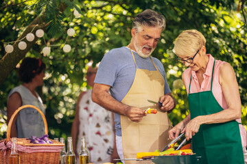 Elderly couple celebrate the 4th of July in their backyard. They are making barbeque, vegetables, and drinking beverages while enjoying and making memories