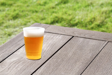 ヴィンテージな木製テーブルの上に置かれたビール。芝生が鮮やかでさわやかな夏の飲み物の演出