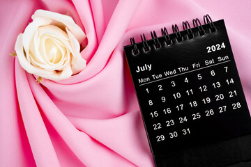 July 2024 desk calendar black color and rose on pink textile background.