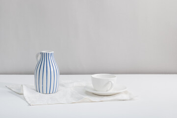 Ceramic jug, vase and empty white cup and saucer on the table.
