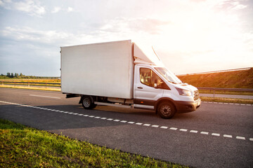 A white light-duty van isotherm transports products between cities on a country road in summer, sunset, industry © HENADZY