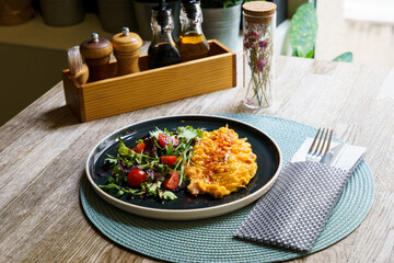 Scrambled eggs with salad and tomato on a wooden table