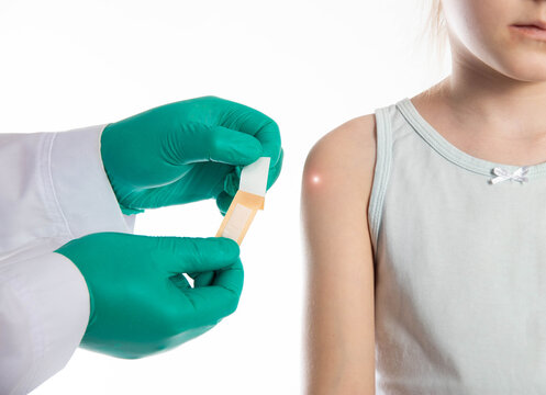 The hands of a doctor in green medical gloves hold a medical plaster against the background of a child s shoulder. Concept of vaccinations against tuberculosis and mumps for children. 