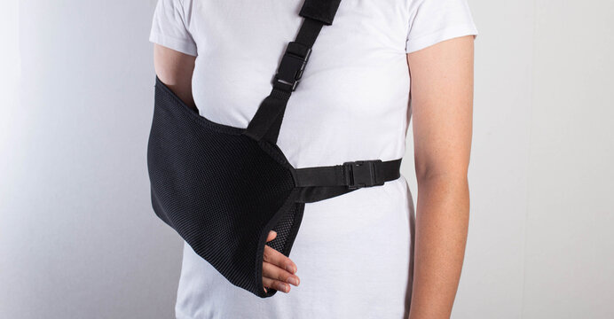 A girl in white with a fixing black bandage on her arm after an injury, a fracture of the radius and a sprain. Arm support bandage, hand immobilization