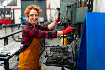 A young woman in STEM uses a machine with a drill before starting work on a new project, using protective equipment and practicing safe work
