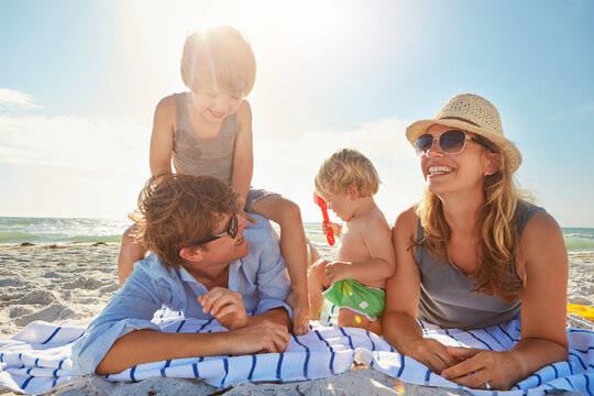 Playing, relax or kids with parents at beach on holiday vacation or happy family weekend together. Father, fun mother or children siblings at sea for bonding or picnic in nature in Spain with love