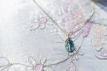 A silver medallion on a chain, placed on a beautiful white fabric embroidered with flowers and butterflies