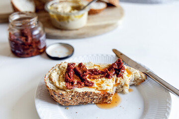 Piece of bread with hummus and sun-dried tomatoes on a white plate. High quality photo