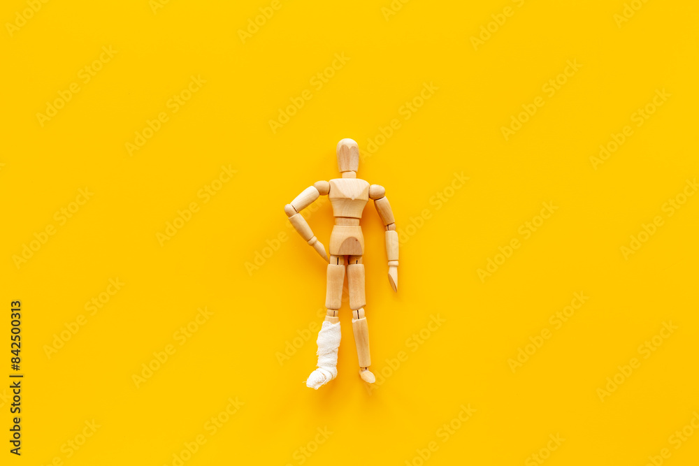 Sticker Wooden dummy man with leg broken - leg in bandage. Medical insurance and healthcare concept