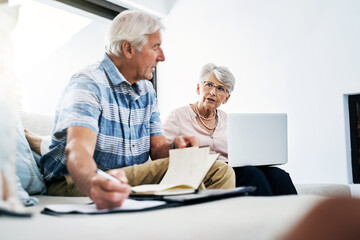 Senior couple, laptop and talking with writing on document in sofa for retirement or shopping list for household. People, planning and budgeting at home for saving, insurance and asset management