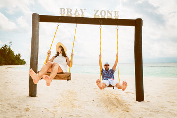 Caucasian couple in love enjoy swings have fun together on beach on summer holidays express emotions being childish and relaxed outdoors together.Cheerful carefree traveling couple