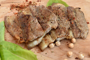 The picture shows thick pieces of bacon fried on green leaves lying on a kitchen board.