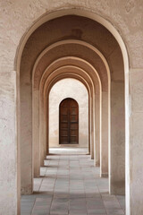 A plain door framed by a series of minimalist arches, each arch slightly larger than the one before, creating a sense of depth and perspective. The background remains solid and neutral